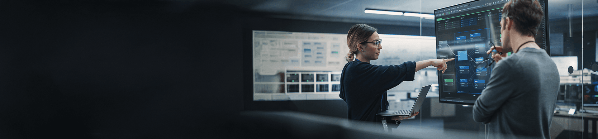 Woman with glasses and laptop pointing at a large data chart.