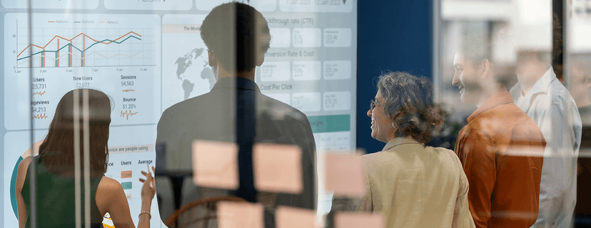 A group of business people look together at a large digital screen displaying various business metrics, charts and key figures.