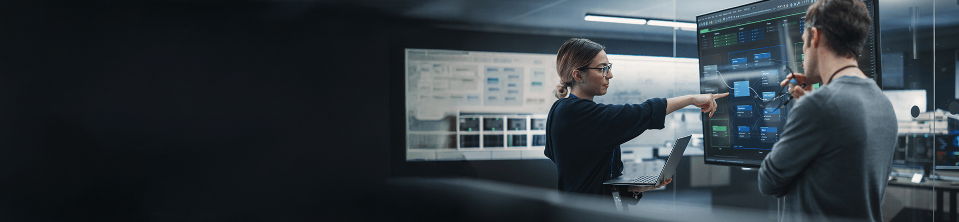 Woman with glasses and laptop pointing at a large data chart.