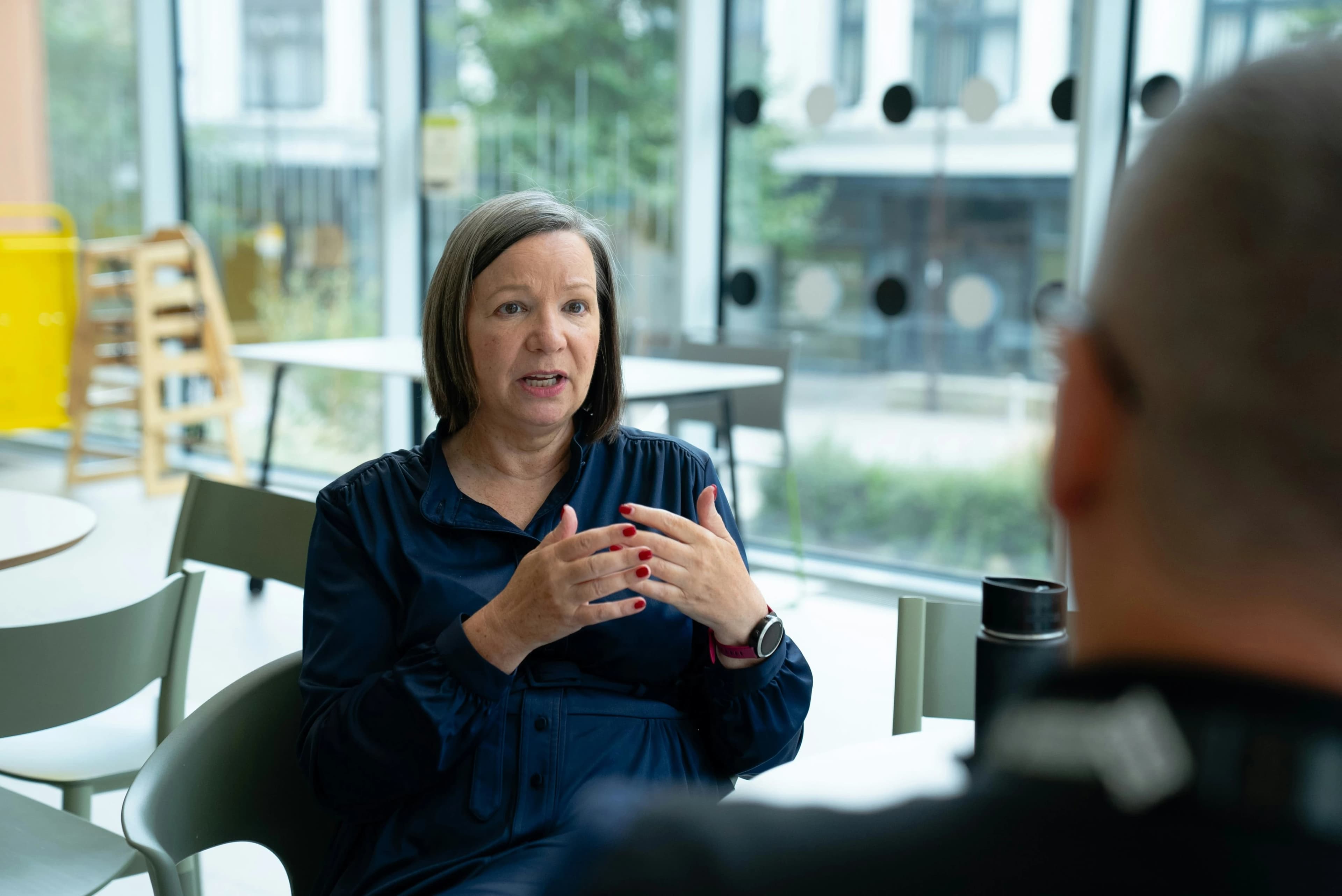 A professional woman gesturing with her hands while speaking to a colleague in a brightly lit, modern office space.